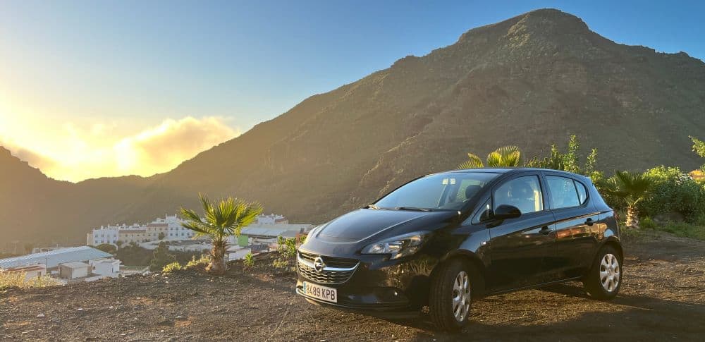 Opel Corsa Mietwagen auf Teneriffa vor einem Berg und Palmen mit blauem Himmel