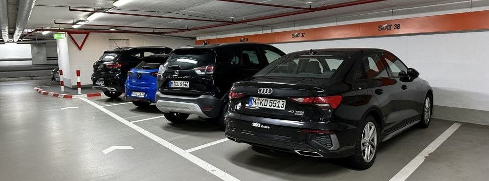 Mehrere Mietwagen verschiedener Hersteller in einer Tiefgarage auf Sixt-Parkplätzen, darunter ein Opel im Hintergrund.